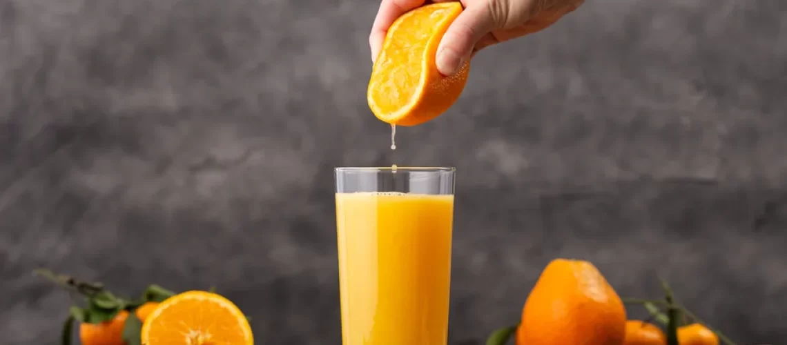 copo-de-suco-de-laranja-e-uma-pessoa-espremendo-uma-laranja-nele