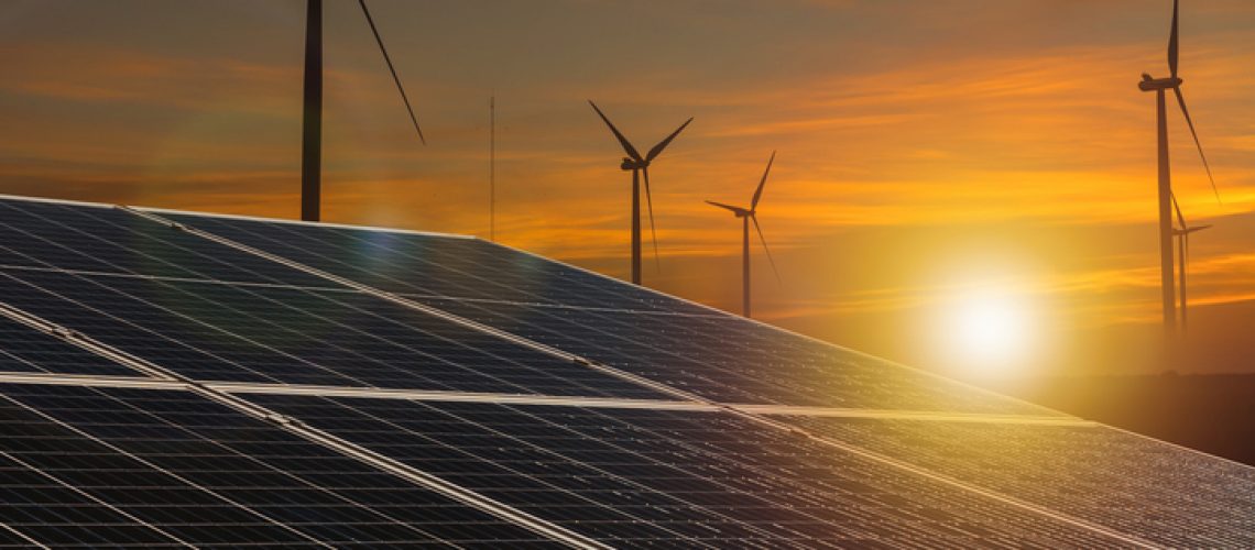 Illuminate your project with this stunning image of renewable energy synergy, capturing solar panels in the foreground with wind turbines silhouetted against the vibrant hues of a setting sun.