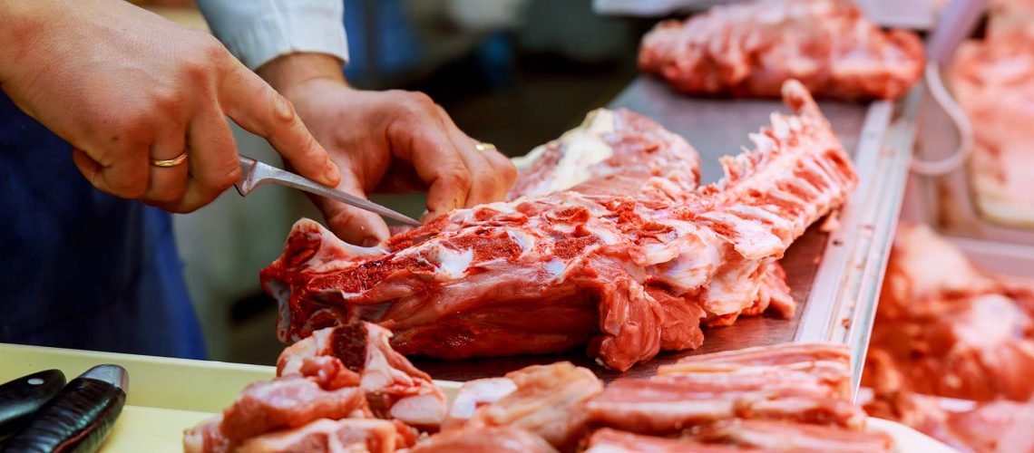 Cropped image of male butcher cutting raw meat with knife at counter in shop